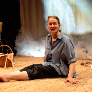 Poster image for "On a House Like Fire". A woman in a loose blue shirt sits on a rug, her legs extended in front of her. She smirks, looking to someone opposite her (unseen).